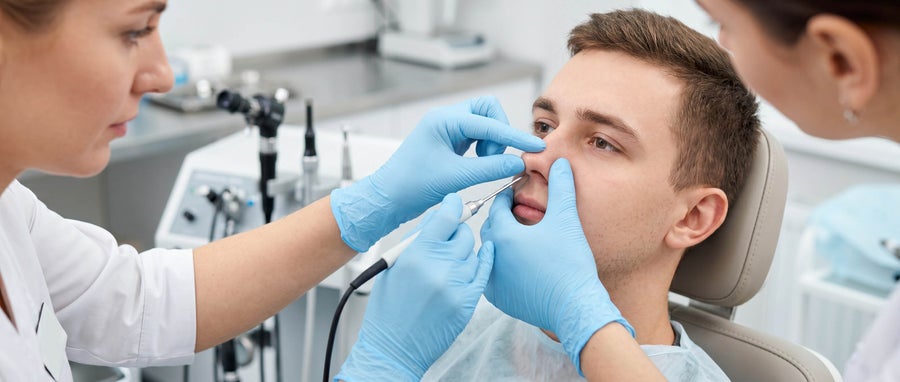 A healthcare worker examines a patient’s nose with an otoscope while wearing blue gloves.