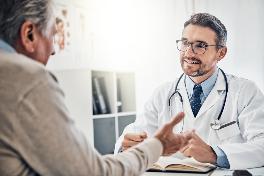 A smiling doctor in a white coat listens attentively while shaking hands with a patient.