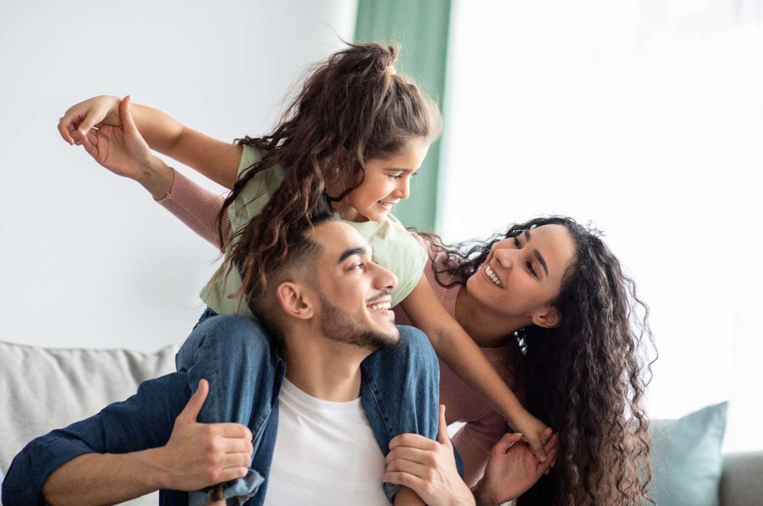A happy family—a man, woman, and young child—laugh seating on sofa