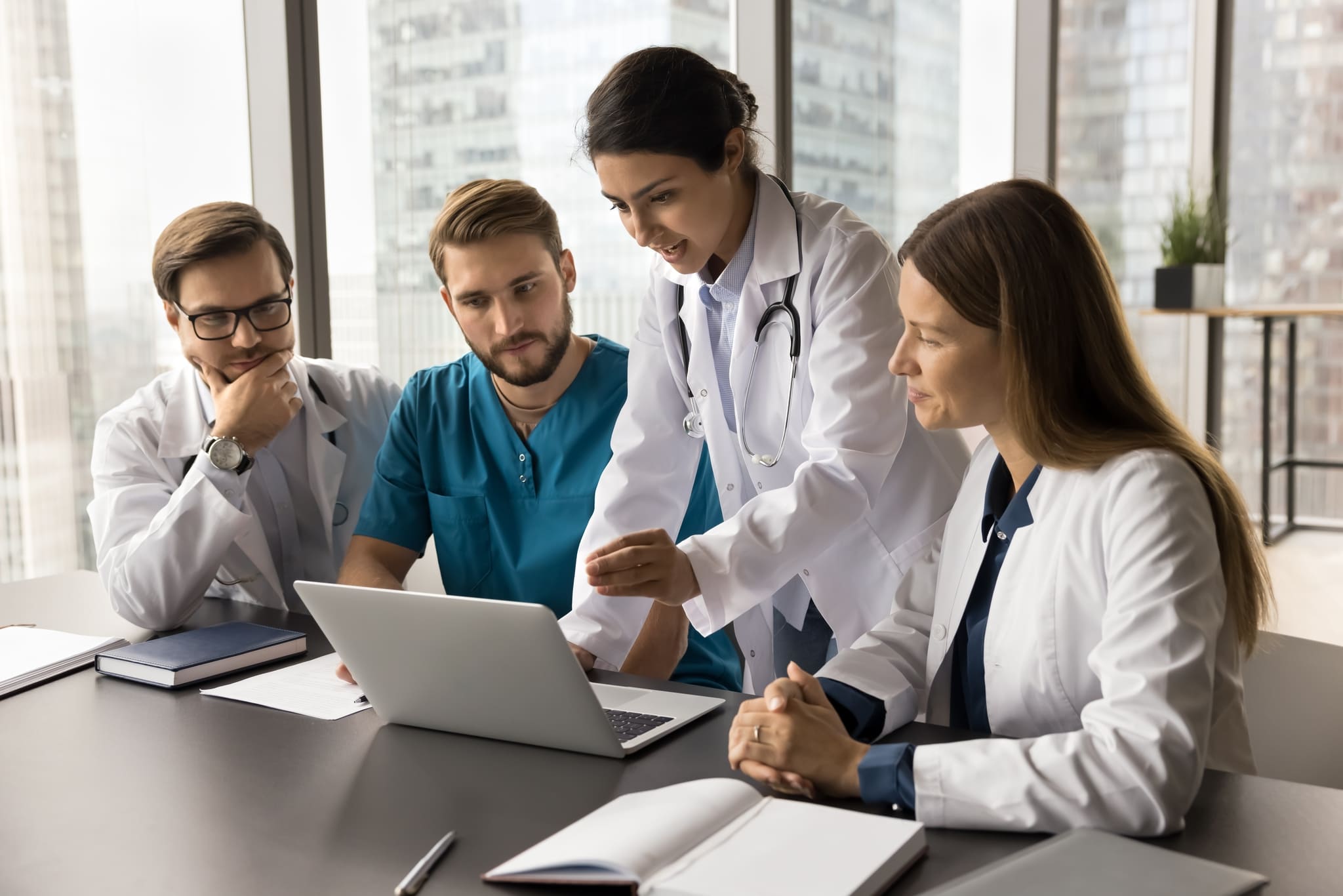 Four medical professionals, two men and two women, collaborate around a laptop in a bright modern office.